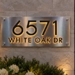 Front view of a brushed stainless steel plaque with raised black 6571 WHITE OAK DR lettering and warm halo backlighting.