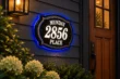 layered classic illuminated sign reading Munday 2856 Place, with white illuminated lettering, gold-tone trim and blue halo beside a wooden door.