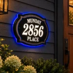 layered classic illuminated sign reading Munday 2856 Place, with white illuminated lettering, gold-tone trim and blue halo beside a wooden door.