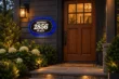 Blue halo illuminated Munday 2856 Place address plaque beside a wooden front door, with a porch lantern and landscaped entrance at dusk.