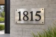 Modern stainless steel address plaque with raised black aluminum numbers on concrete wall