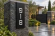 Vertical black aluminum address sign 918 with brushed silver numbers on a stone pillar