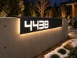 Bent aluminium 4438 address sign mounted over a concrete wall edge beside a modern home entrance.