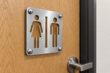 Angled view of cut-through brushed aluminium washroom sign with four domed mounting caps