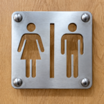 Close-up of brushed aluminium washroom sign with cut-through male and female symbols on an oak door