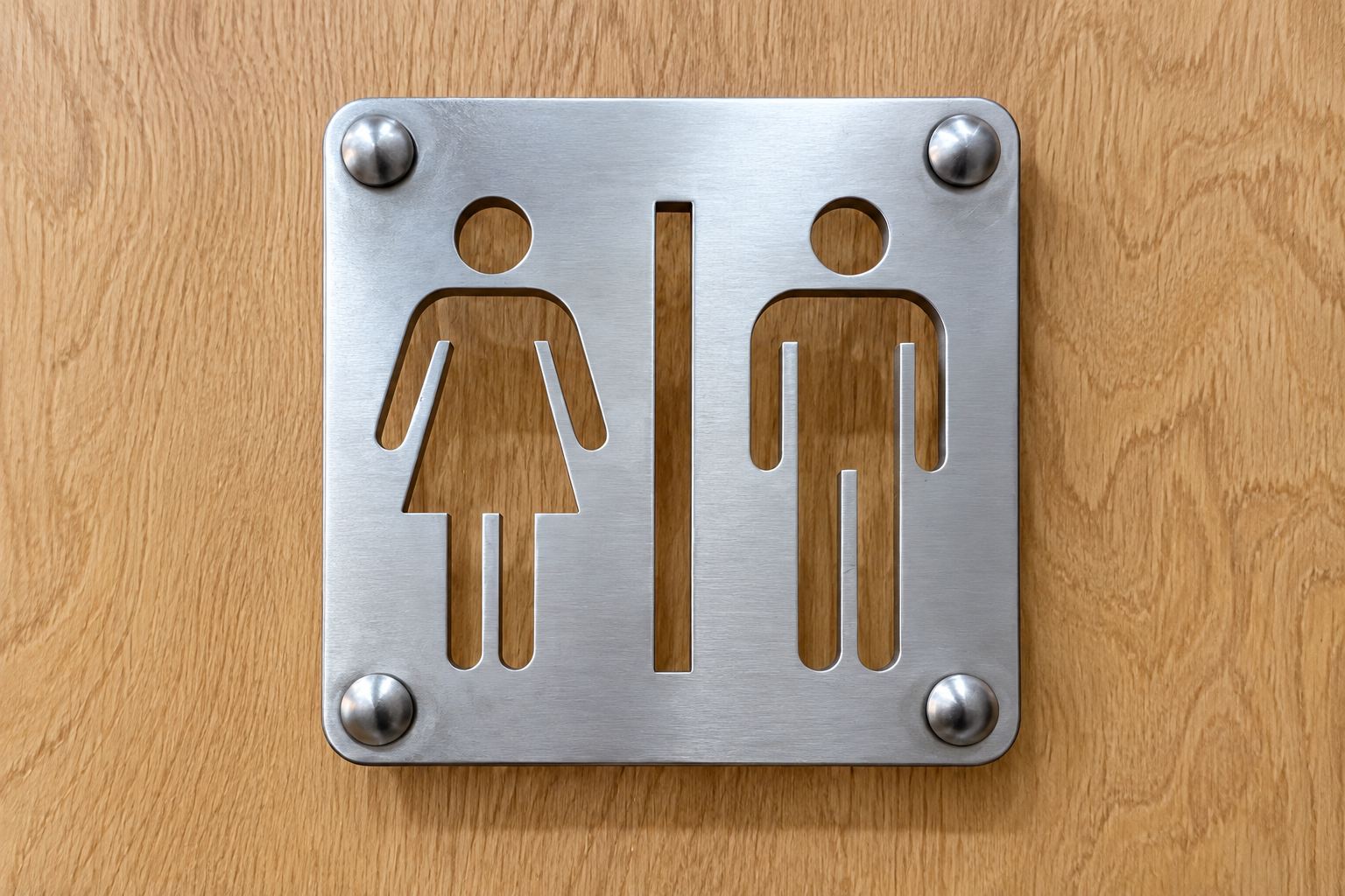 brushed-aluminium-washroom-sign-close-up Close-up of brushed aluminium washroom sign with cut-through male and female symbols on an oak door
