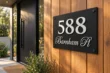 Custom brushed silver house numbers 588 and Barnham Pl on a matte black panel beside a cedar entrance