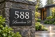 Modern brushed silver address sign 588 on a matte black panel mounted to a stone pillar
