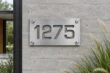 See-through brushed aluminum address sign 1275 mounted on a contemporary concrete wall
