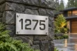 See-through brushed aluminum house number sign 1275 mounted on a stone pillar